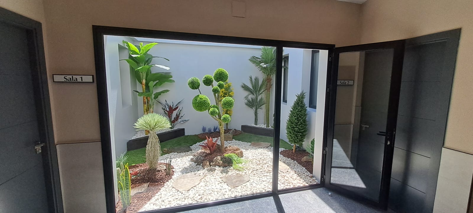 Patio de luces con jardín artificial de suelo: platanera, topiario, palmera y grava