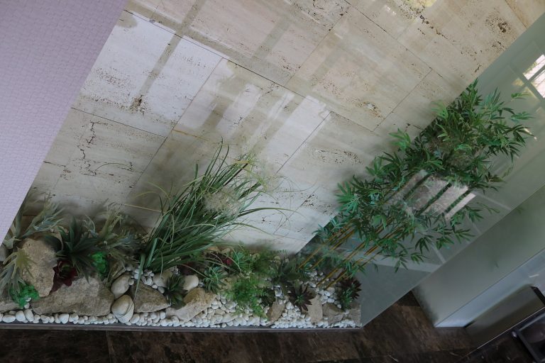 Jardinera de interior con gramíneas y bambú junto a pared de travertino