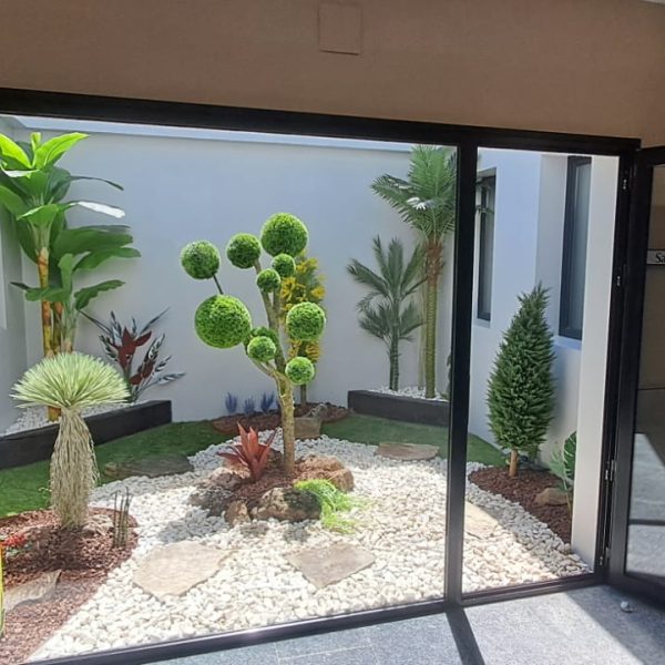 Patio de luces con jardín artificial de suelo: platanera, topiario, palmera y grava